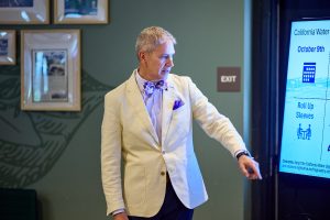 A man in a white blazer makes a presentation using a screen at a meeting