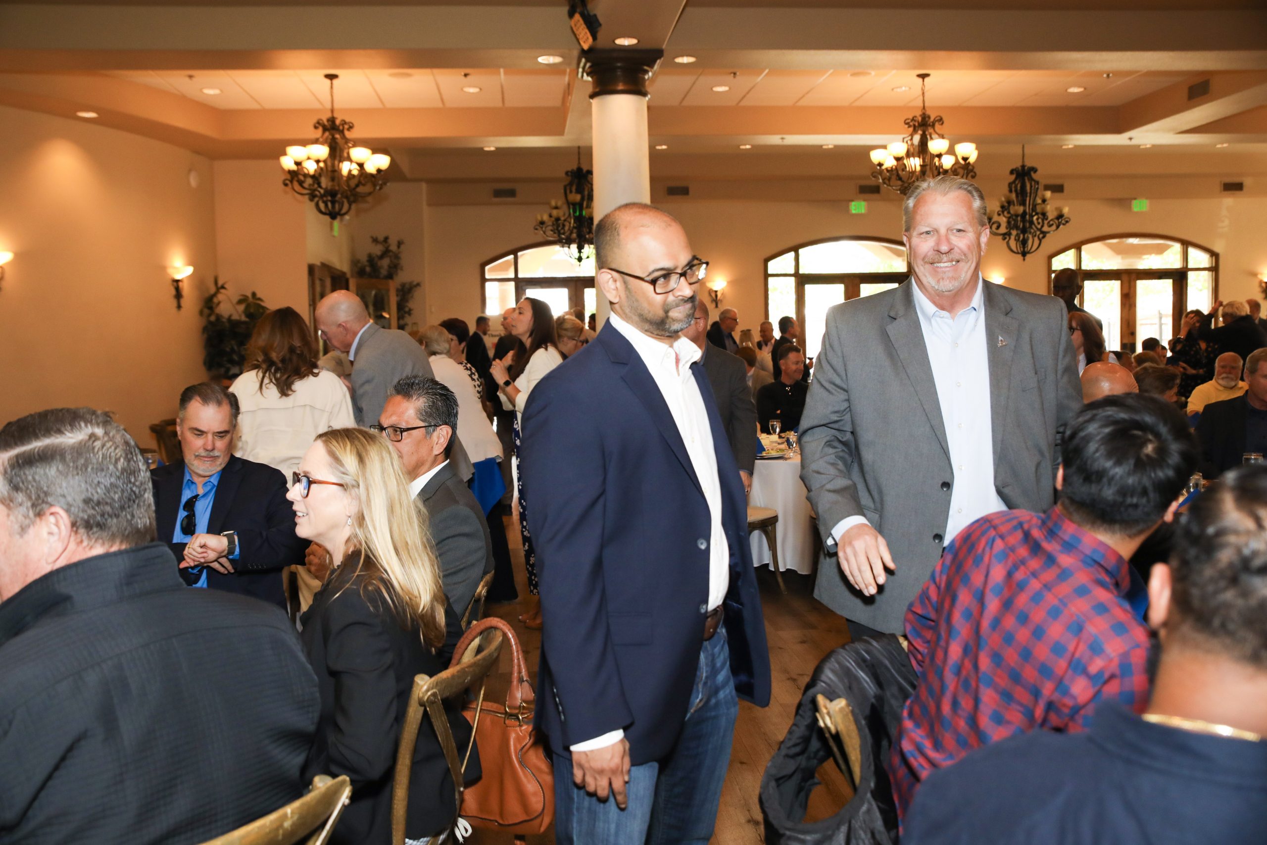 Two men in business attire network in a crowded room at the Southern California Water Coalition luncheon